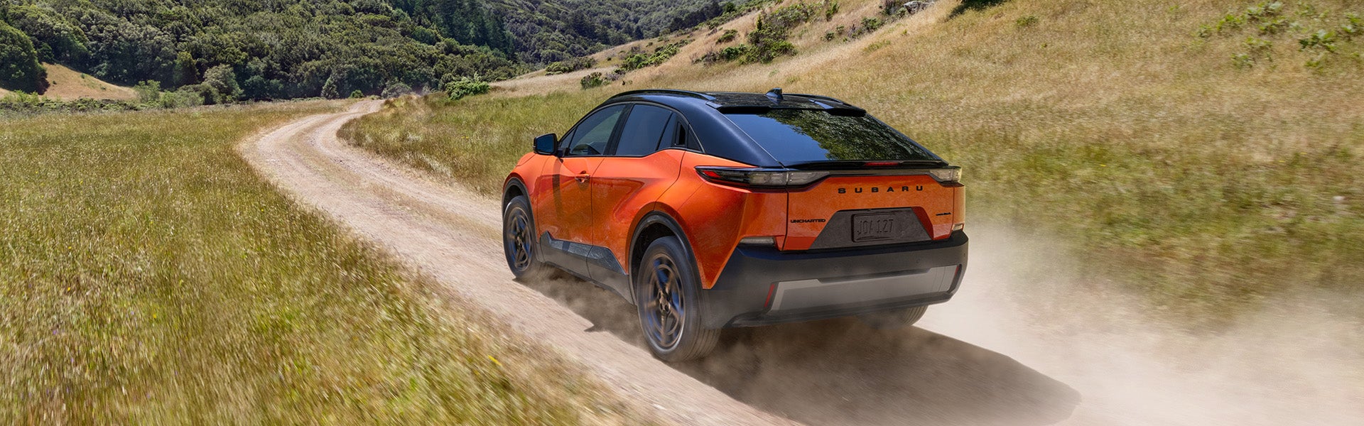 Rear driver-side view of a Subaru EV SUV heading down a mountain road